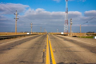 Road by electricity pylon against sky