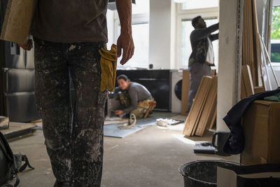 Midsection of carpenter carrying plank while coworkers working in kitchen at home