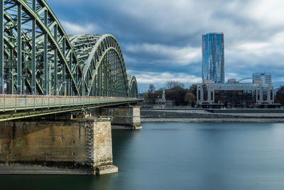 Bridge over river in city against cloudy sky