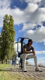 Full length of man sitting at park against sky