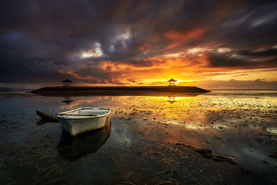 Boat moored on beach against sky during sunset