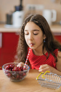 Teenage girl drinks juice from a cherry in a plate through a straw. the concept of an organic