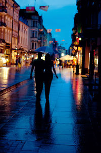 Rear view of woman walking on wet street at night