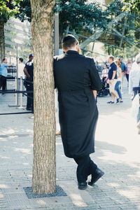 Rear view of man leaning on tree