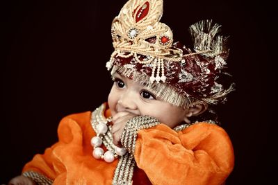 Close-up of baby boy wearing traditional clothing against black background