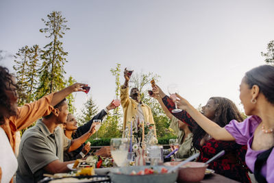 Multiracial male and female friends toasting drinks while celebrating during dinner party in back yard