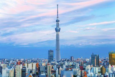 Communications tower in city against cloudy sky