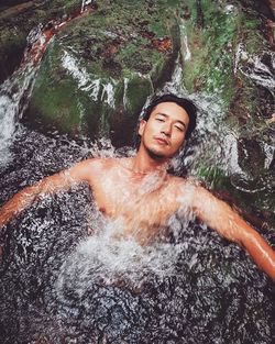Portrait of shirtless young man looking at waterfall