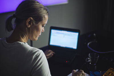 Female it professional writing while working on laptop in creative office