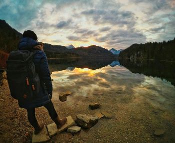 Rear view of people standing by lake against sky during sunset