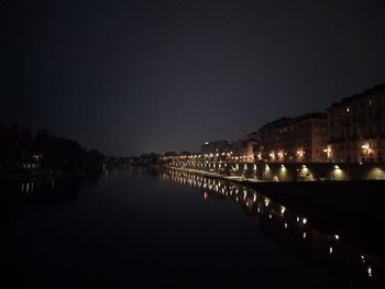 Illuminated city by river against clear sky at night