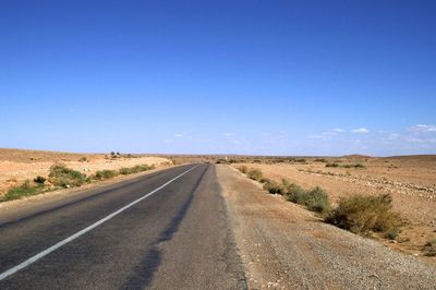 Road leading towards landscape against blue sky