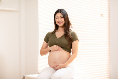 Young woman smiling while sitting against wall