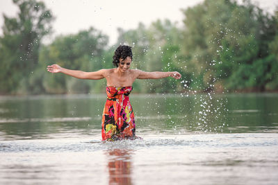 Full length of shirtless man splashing water in lake