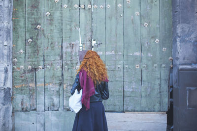 Rear view of woman standing in front of wooden wall