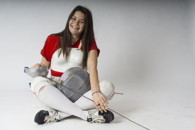 Portrait of smiling young woman with sword and headwear sitting against white background