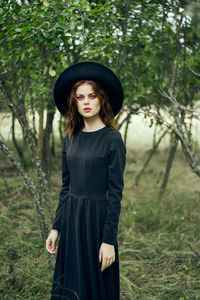 Portrait of young woman standing against trees