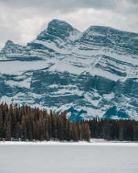 Scenic view of frozen lake with trees and snowcapped mountains against sky