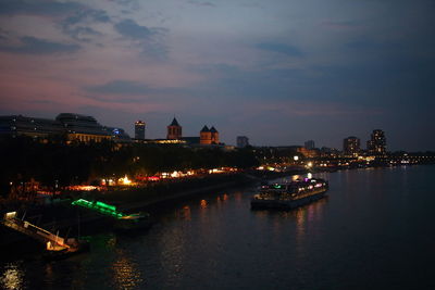 Illuminated buildings by river against sky in city at night