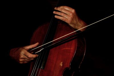 Close-up of man playing cello against black background