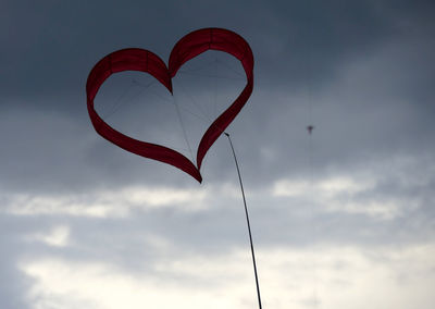 Low angle view of red heart shape kite flying against sky