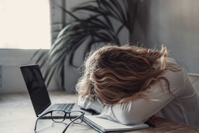 Rear view of woman using laptop at home