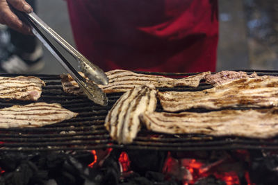 Woman grilling slices of pork steaks febras on the street during the feasts of the popular saints