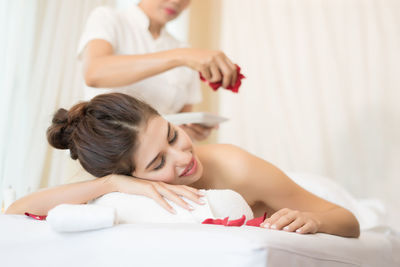 Masseur putting flower petals on young woman in spa