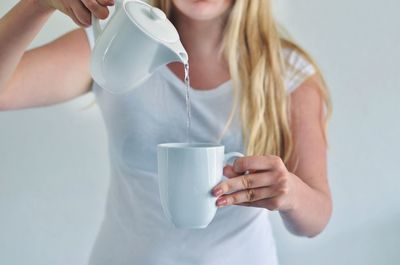 Midsection of woman pouring water in cup against white background
