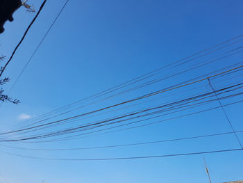 Low angle view of power cables against clear blue sky