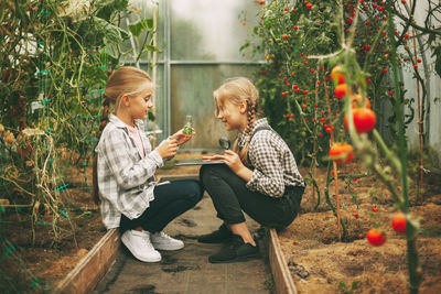 Two cute girls with a tablet in their hands examine a sample of a plant through a magnifying glass. 