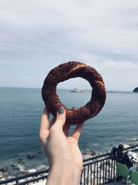 Human hand holding sea against sky