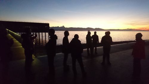 Silhouette people standing on beach against sky during sunset