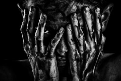 Portrait of boy covering face with hands against black background