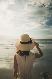 Rear view of woman standing on beach against sky