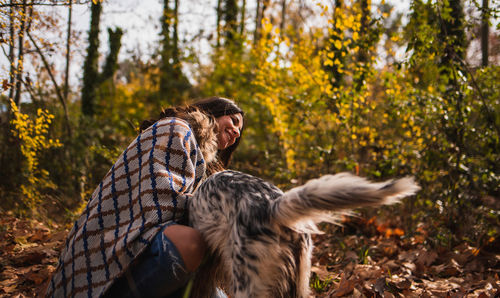 General shot of a beautiful woman playing with her dog in a forest full of leaves.