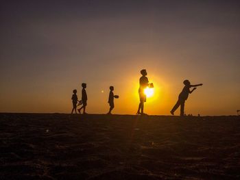 Silhouette people standing on beach against sky during sunset