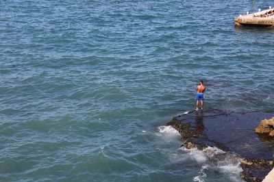 High angle view of man standing on rock in sea