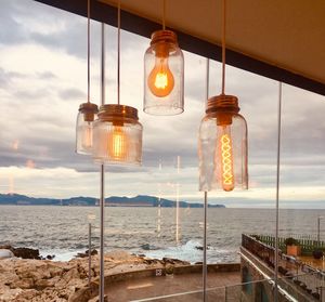 Illuminated light fixtures hanging against window with sea in background