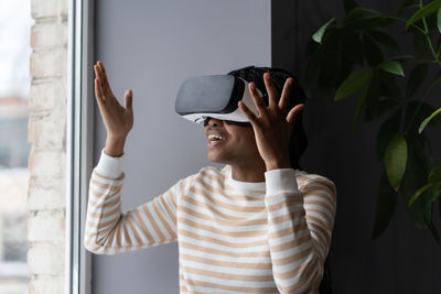 Stunned amazed young african woman gesturing in excitement while using vr headset glasses at home