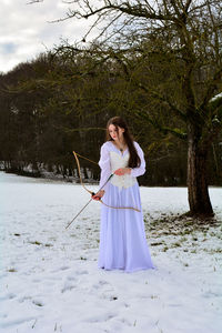 Full length of woman standing on field in snow with a bow 