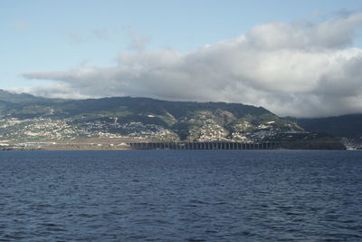 Scenic view of sea by mountain against sky