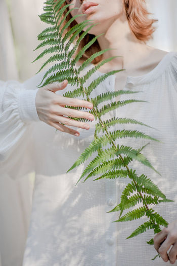 MIDSECTION OF WOMAN HOLDING PLANT IN SUNLIGHT