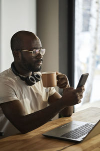 Man using smart phone holding tea cup sitting at home