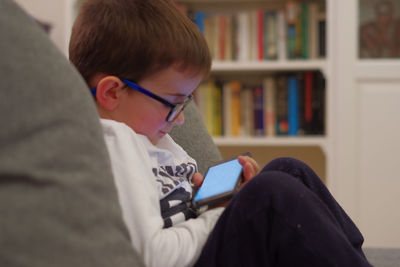 Side view of boy looking at smart phone while sitting at home