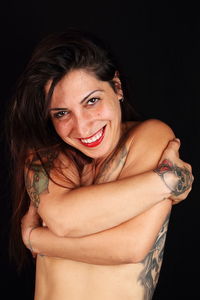 Portrait of shirtless woman with tattoos covering breast against black background