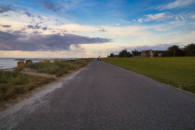 Road amidst field against sky during sunset