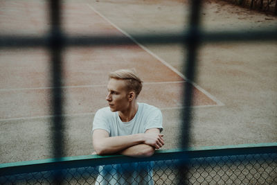 Young man standing by fence on court