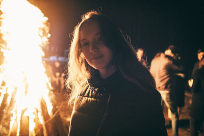 Portrait of young woman standing near campfire on field at night