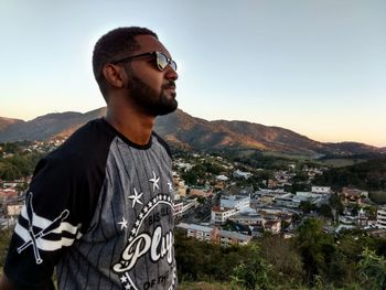 Young man wearing sunglasses standing by cityscape against sky